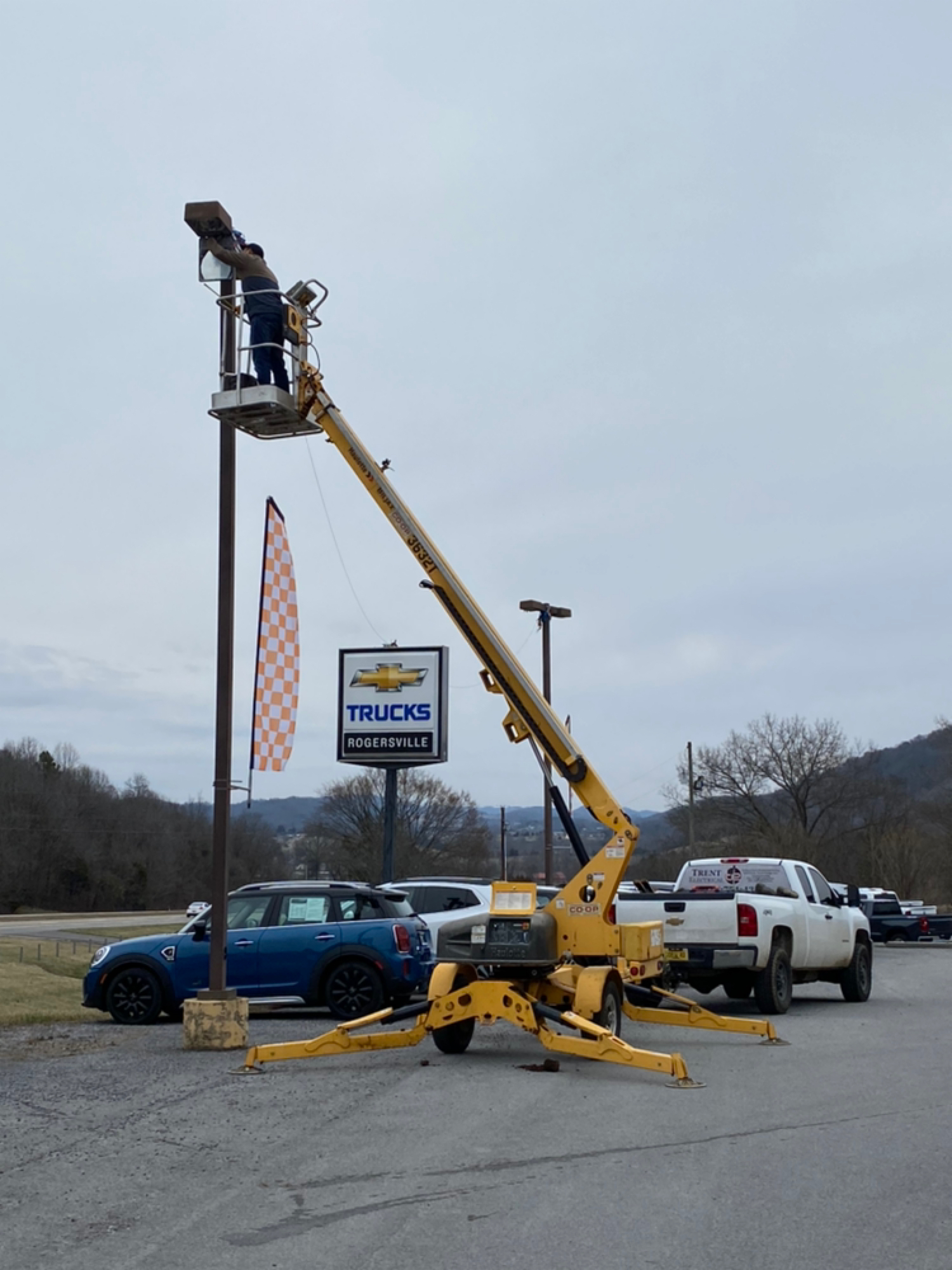 Electrician servicing a tall parking lot light pole from a bucket lift at a commercial property