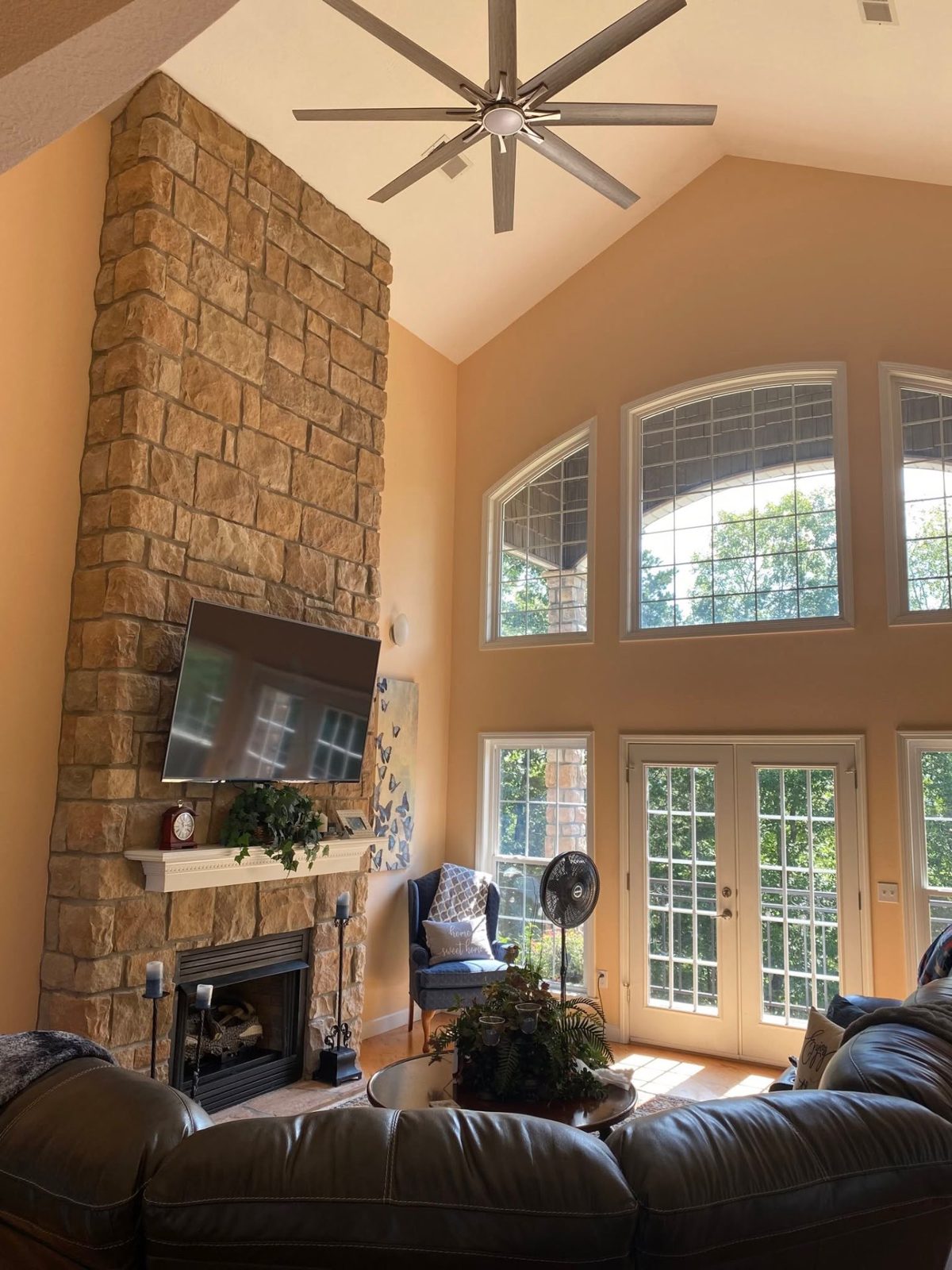 Large ceiling fan installed on a high vaulted ceiling above a stone fireplace