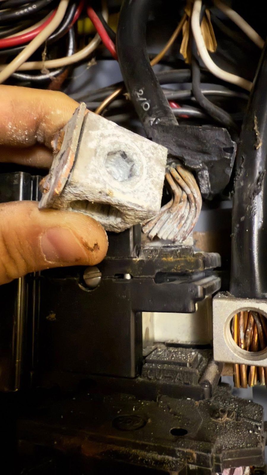 Electrician holding a damaged overheated lug connector removed from a panel