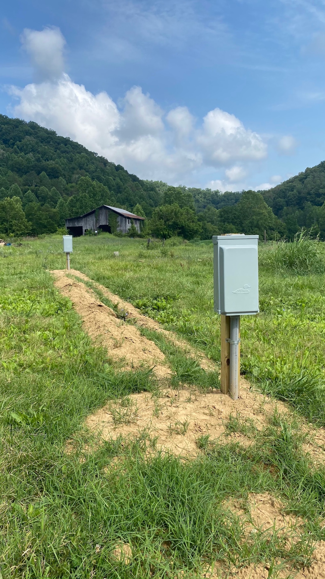 Two electrical pedestals set along a freshly dug underground service trench in a rural East Tennessee field