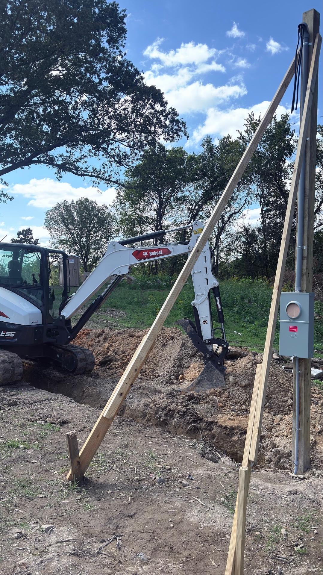 Mini excavator digging a service trench beside a newly set electrical pole in Hawkins County TN