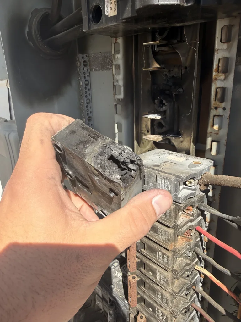 Removed breaker with severe burning at its connection end, held in front of the existing Surgoinsville panel