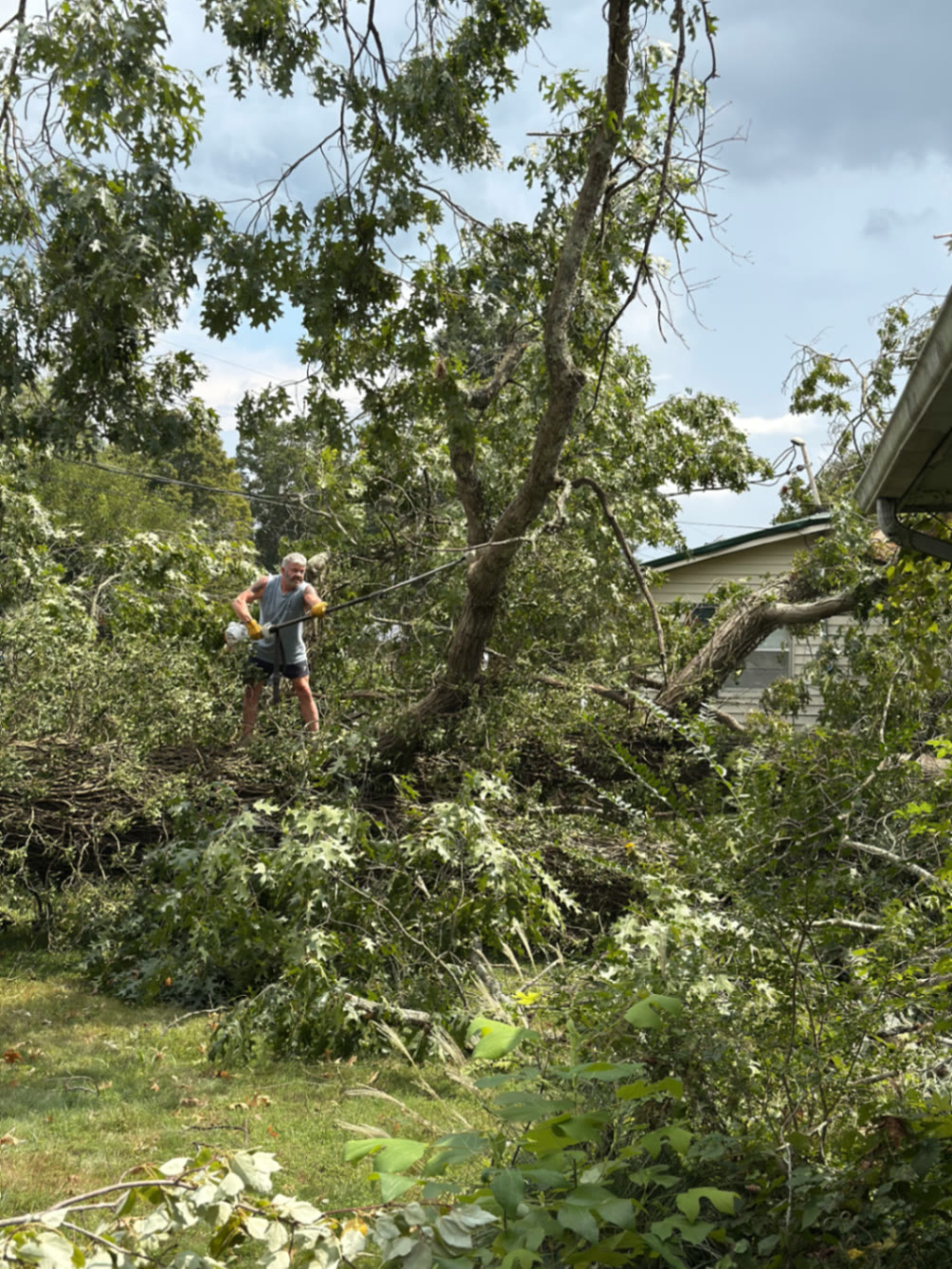 Clearing storm-down tree limbs away from a home's overhead electrical service drop