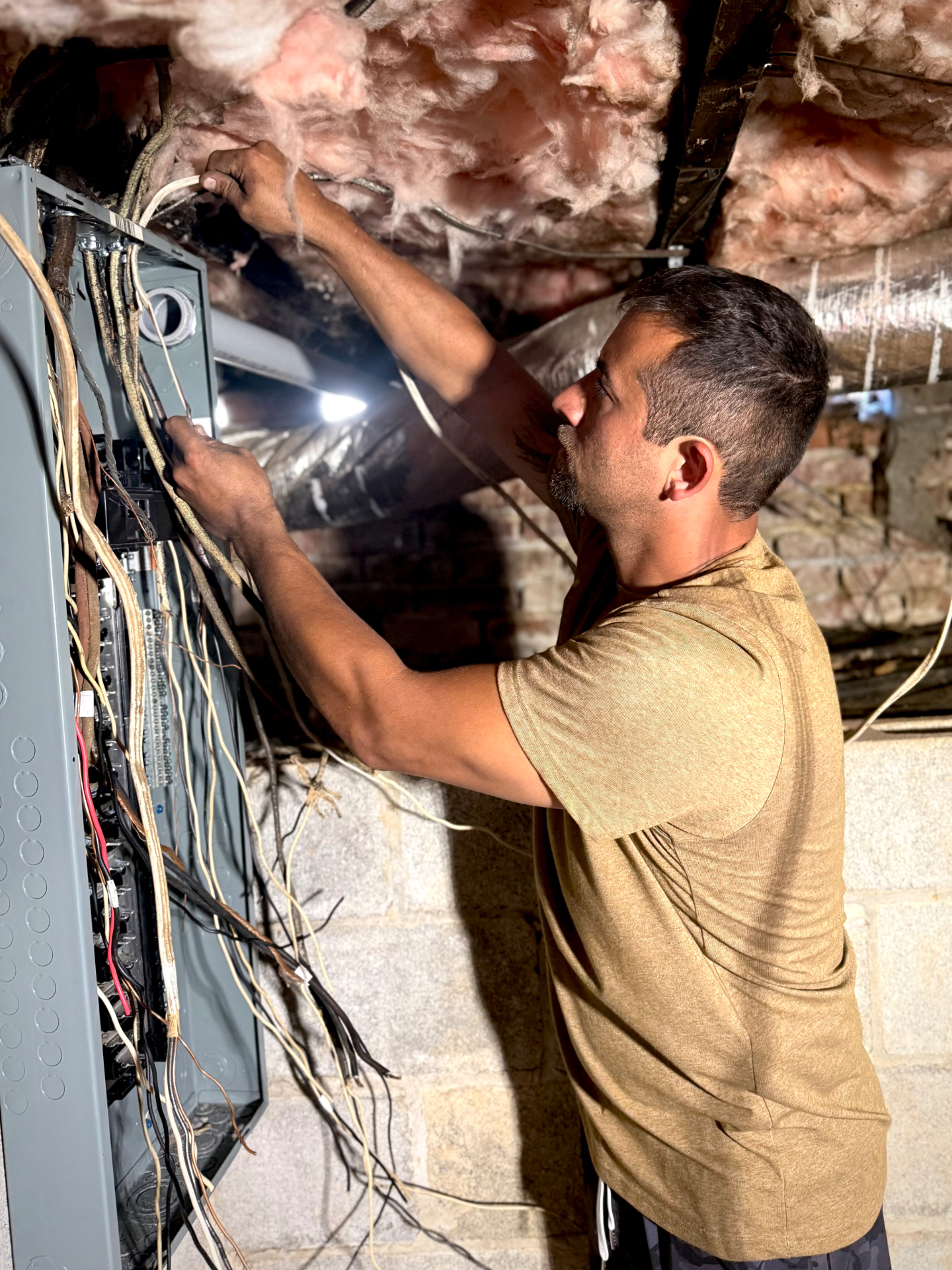 Ryan Trent troubleshooting and pulling new circuits at an open electrical panel in an East Tennessee crawlspace