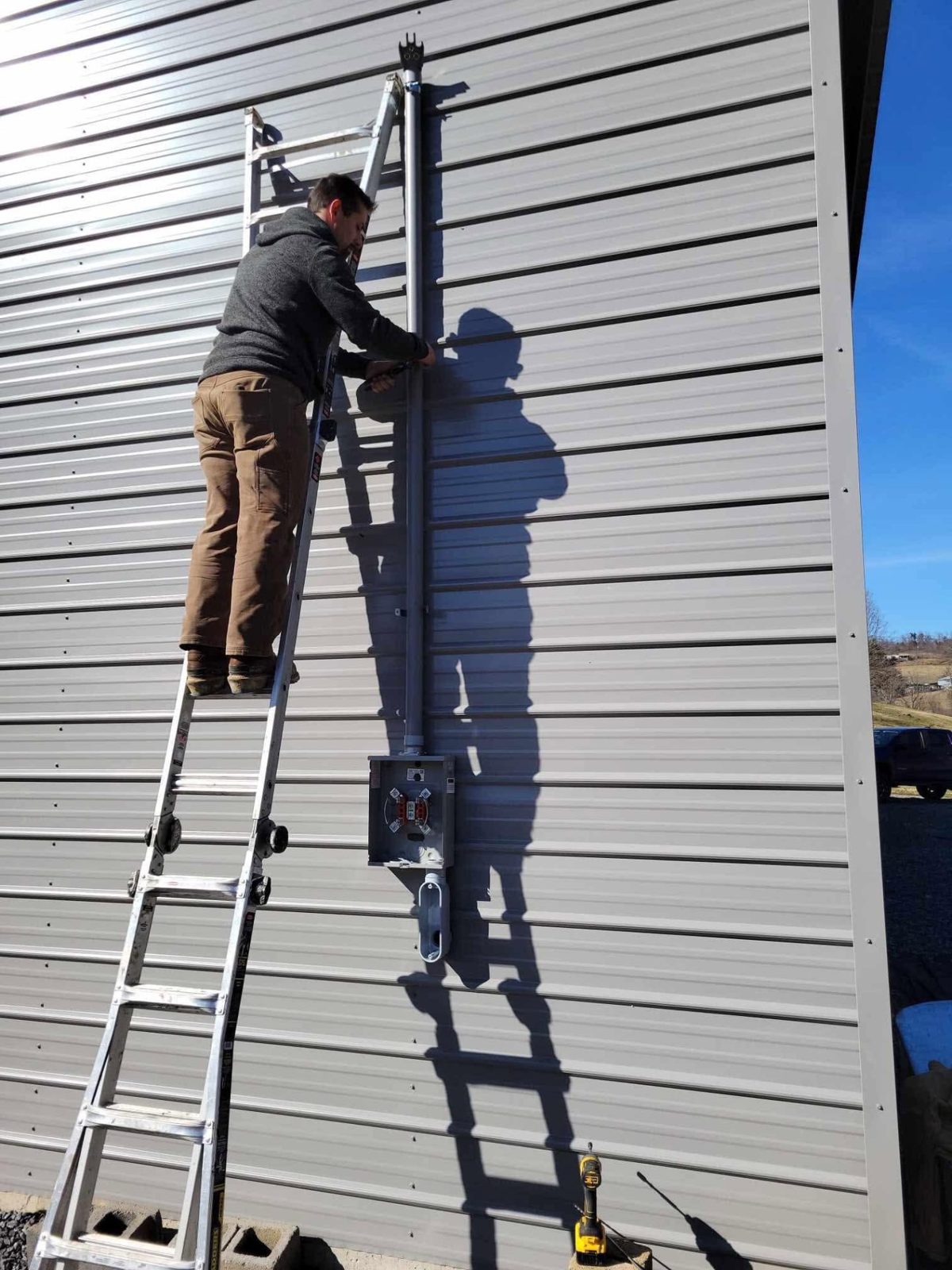 Electrician on a ladder installing a service mast on the side of a metal building in East Tennessee