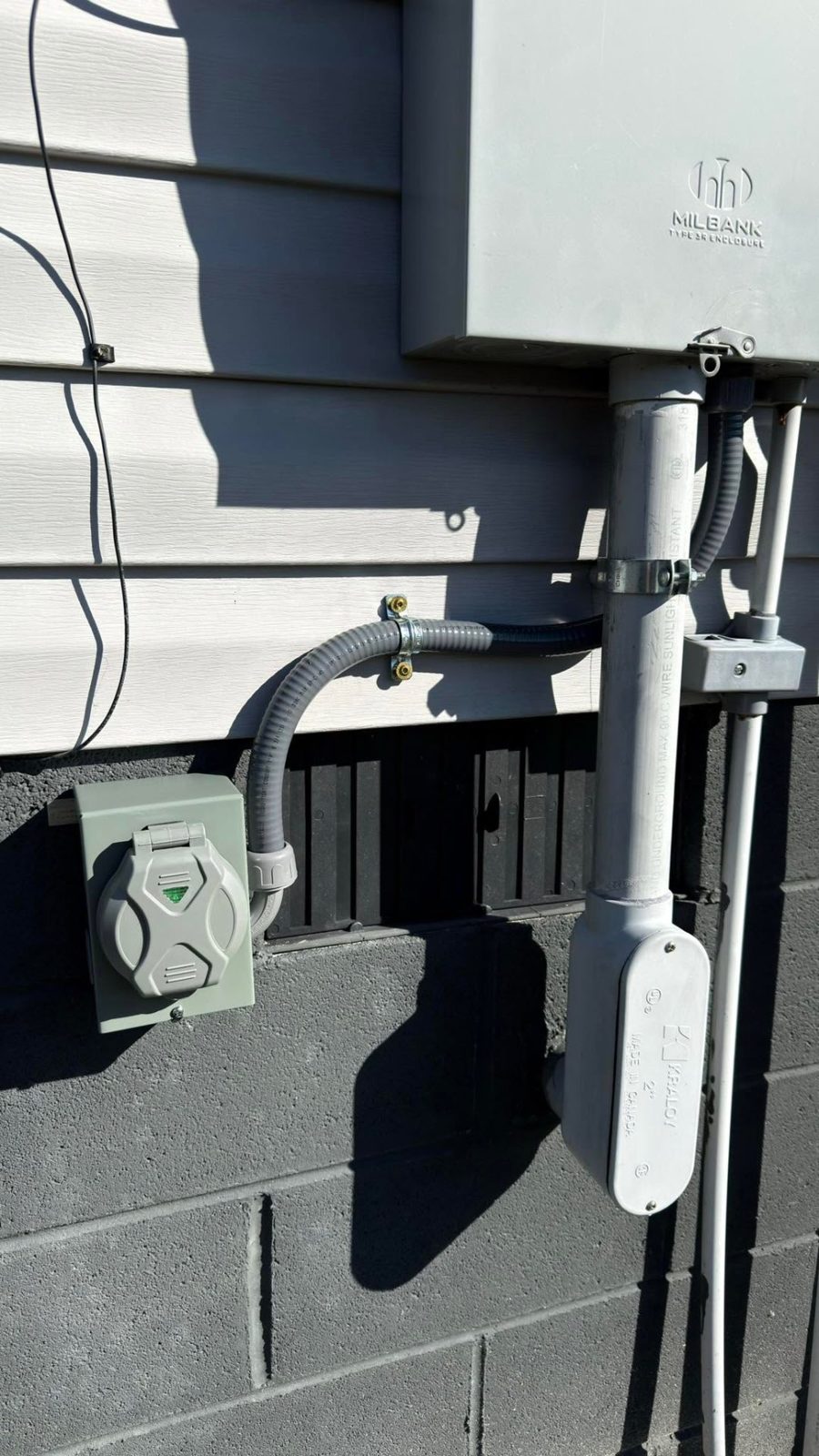 Exterior weatherproof outlet and meter base mounted on a brick and siding wall