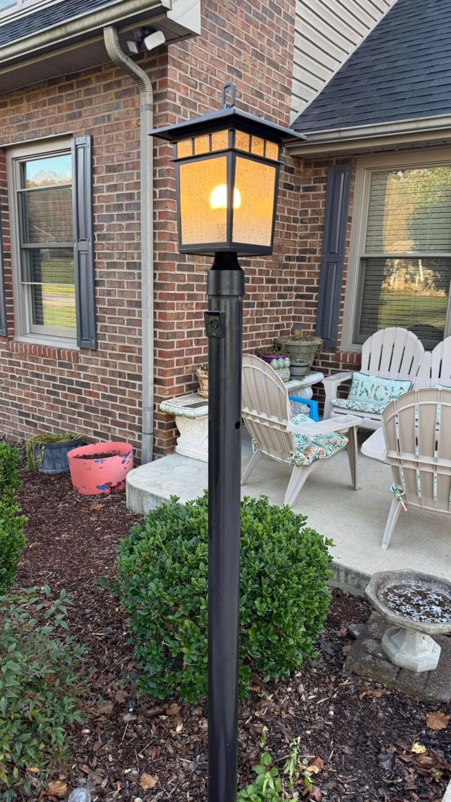 Black lantern style lamp post lit on a brick patio at night